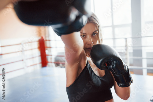 Never surrender. Female sportswoman training in the boxing ring. In black colored clothes