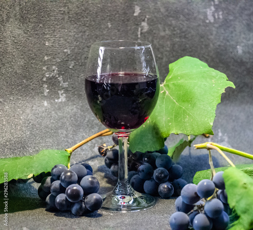 Grapes in a glass with wine on a black background. Grones of grapes with green leaves.. photo