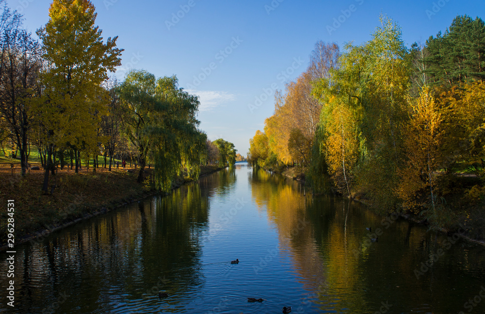 Autumn park with yellow leaves and trees with a river and reflection in the water and blue sky. Autumn park with yellow leaves and trees with a river and reflection in the water and blue sky.