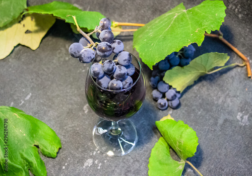 Grapes in a glass with wine on a black background. Grones of grapes with green leaves.. photo