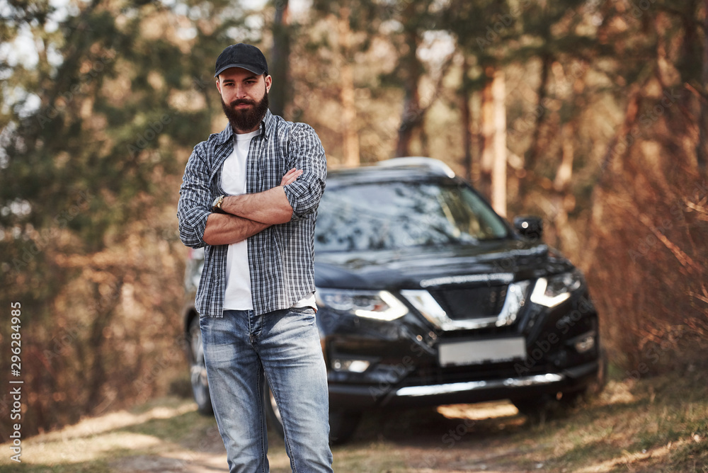 Confident look. Bearded man near his brand new black car in the forest. Vacations concept Confident look. Bearded man near his brand new black car in the forest. Vacations concept