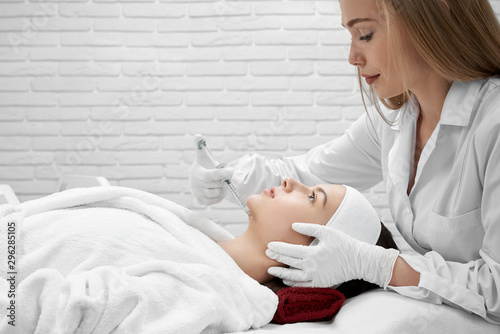 Cosmetologist leaning over face of woman, making injection.