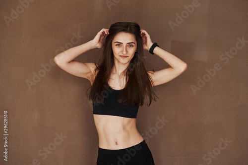Ready for the fitness exercises. Young beautiful woman standing in the studio against brown background