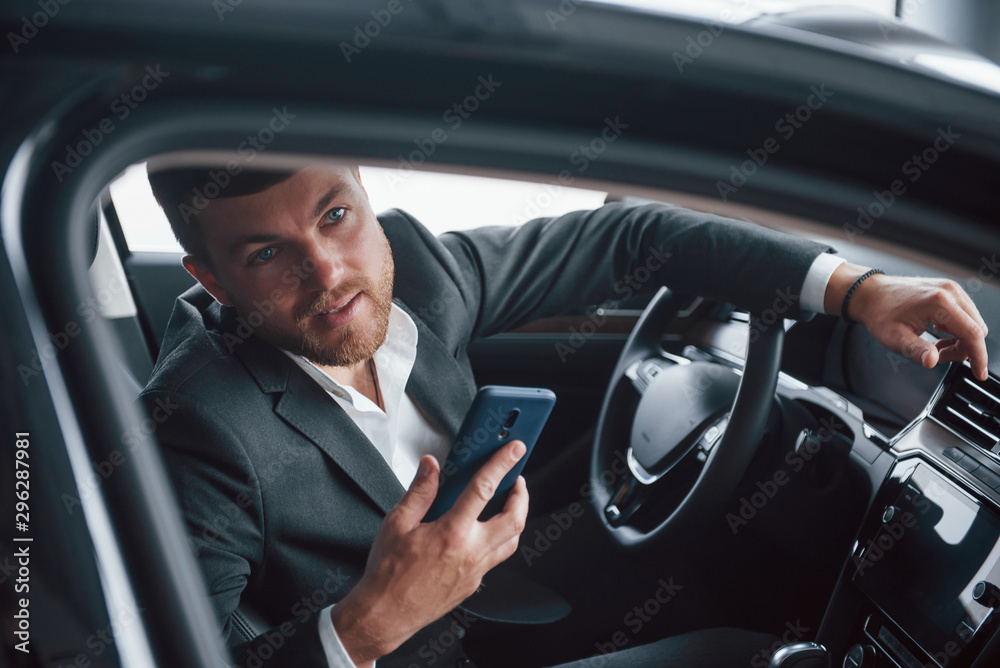 Looking through the window. Modern businessman trying his new car in the automobile salon Looking through the window. Modern businessman trying his new car in the automobile salon