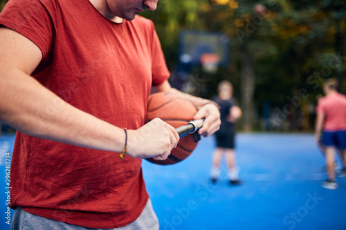 Man inflating basketball ball with a hand pump on the urban court. photo