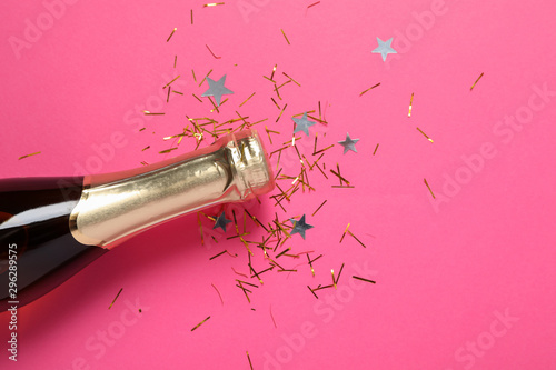 Champagne bottle and glitter on pink background, close up