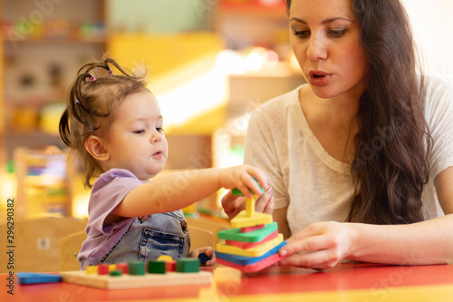 Teacher and kid girl playing colorful block toys in creche