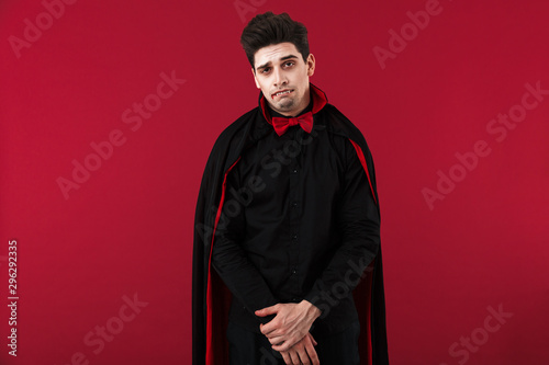 Fotografie Image of sad vampire man with blood and fangs in black halloween costume