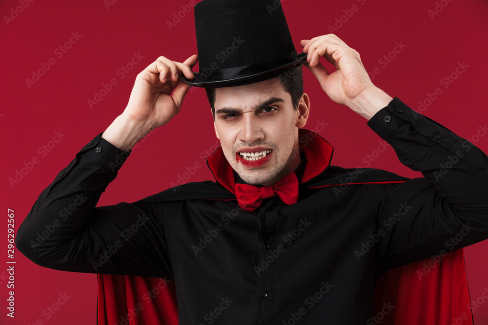 Image of vampire man with fangs in black halloween costume wearing hat Image of vampire man with fangs in black halloween costume wearing hat