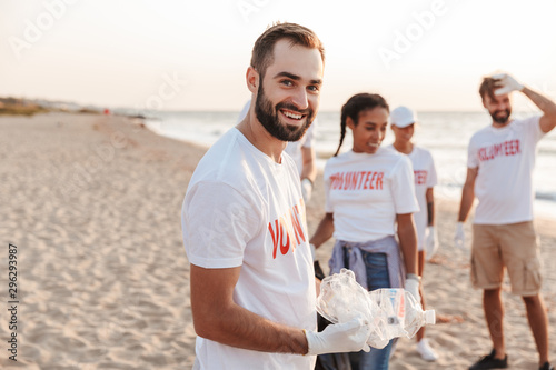 Image of multinational eco volunteers cleaning beach from plastic at seashore