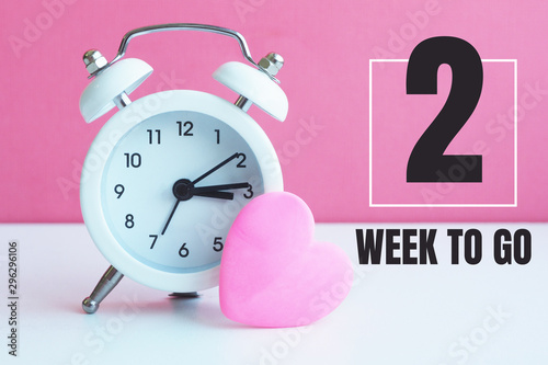 A small white alarm clock and a pink heart figurine. The inscription 