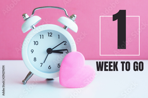 A small white alarm clock and a pink heart figurine. The inscription 