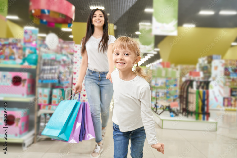 Girl keeping hand of mom and running forwardn in toy store Girl keeping hand of mom and running forwardn in toy store