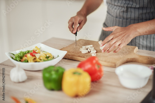 Close up of mixed race woman in apron standing in kitchen and chopping mushrooms.