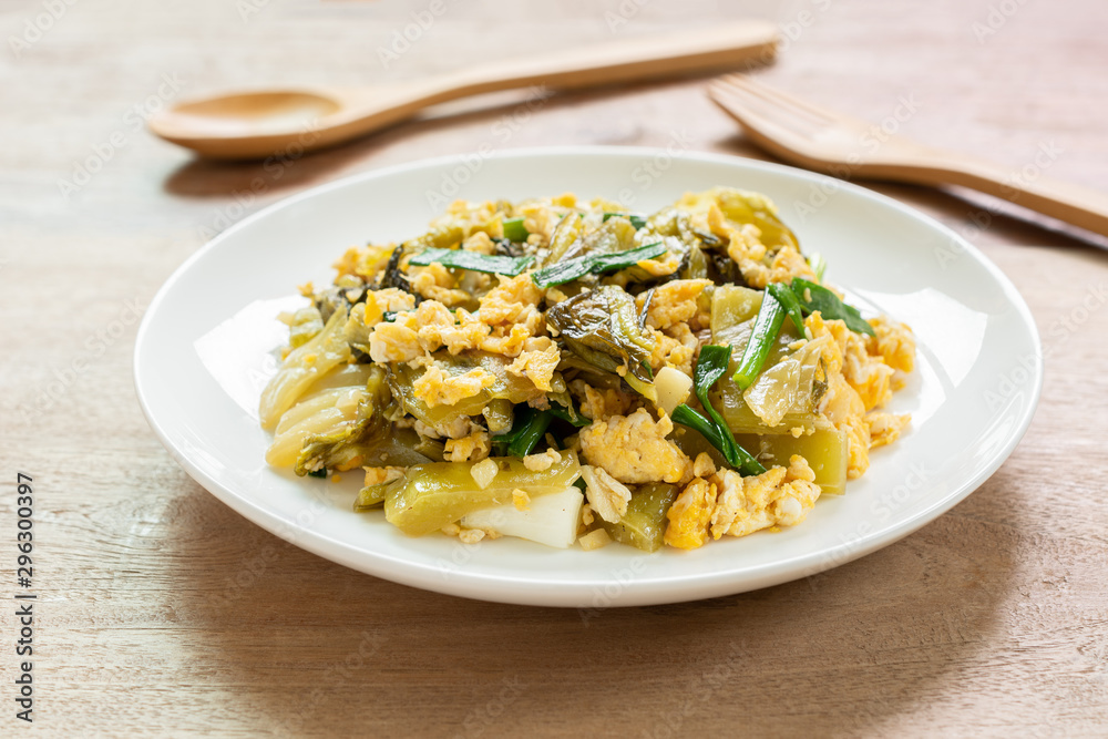 close up of stir fried pickled mustard green with egg in a ceramic dish on wooden table. asian homemade style food concept. close up of stir fried pickled mustard green with egg in a ceramic dish on wooden table. asian homemade style food concept.