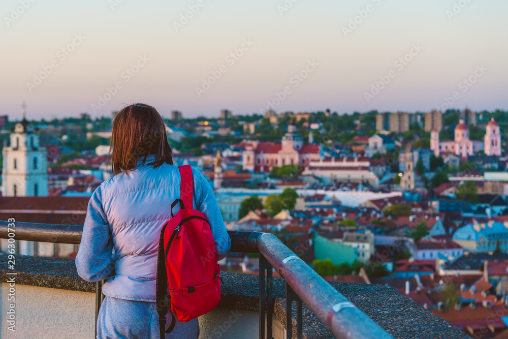 Young woman traveling with the bright red backpack watching sunset in the city