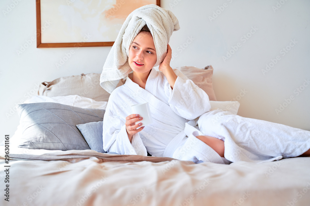 Image of young woman in white coat with a glass of coffee in her hands lying on bed. Image of young woman in white coat with a glass of coffee in her hands lying on bed.