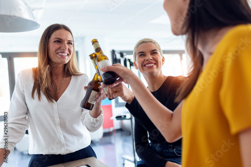 Sticker Three young entrepreneur women toasting with a bottle of beer to celebrate a success in the office