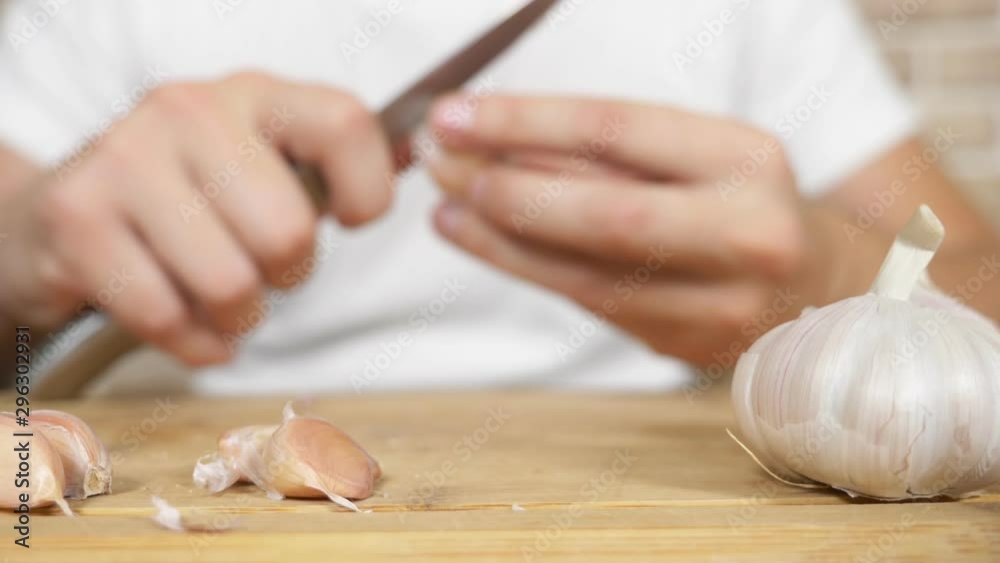 closeup head of garlic, male hands peel the garlic on a wooden board closeup head of garlic, male hands peel the garlic on a wooden board