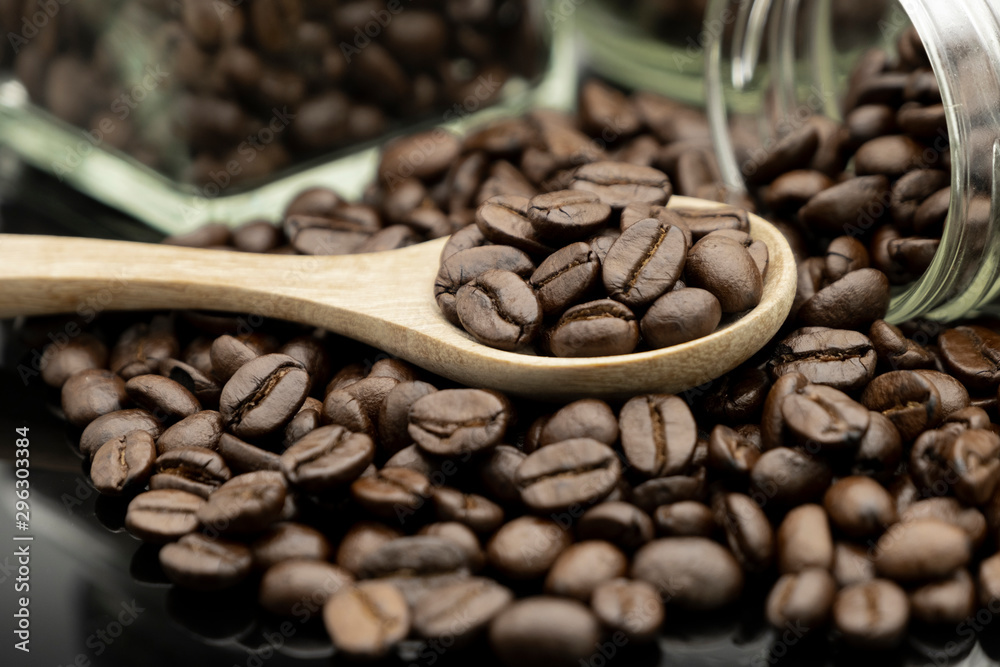 Fototapeta premium Roasted coffee beans in wooden spoon and spread on black table with bottle glass