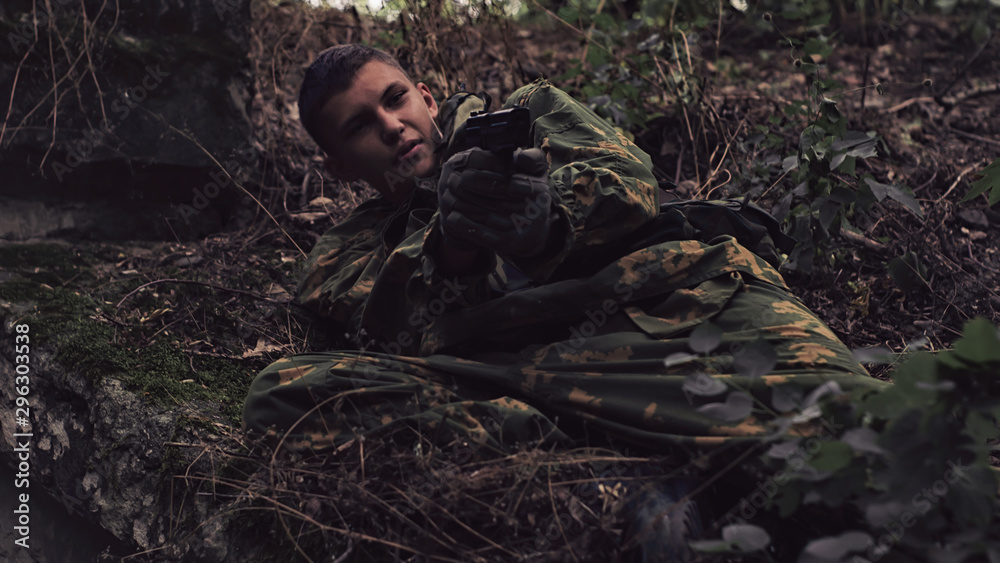 armed man in camouflage clothes in the forest with a gun lies on the ground