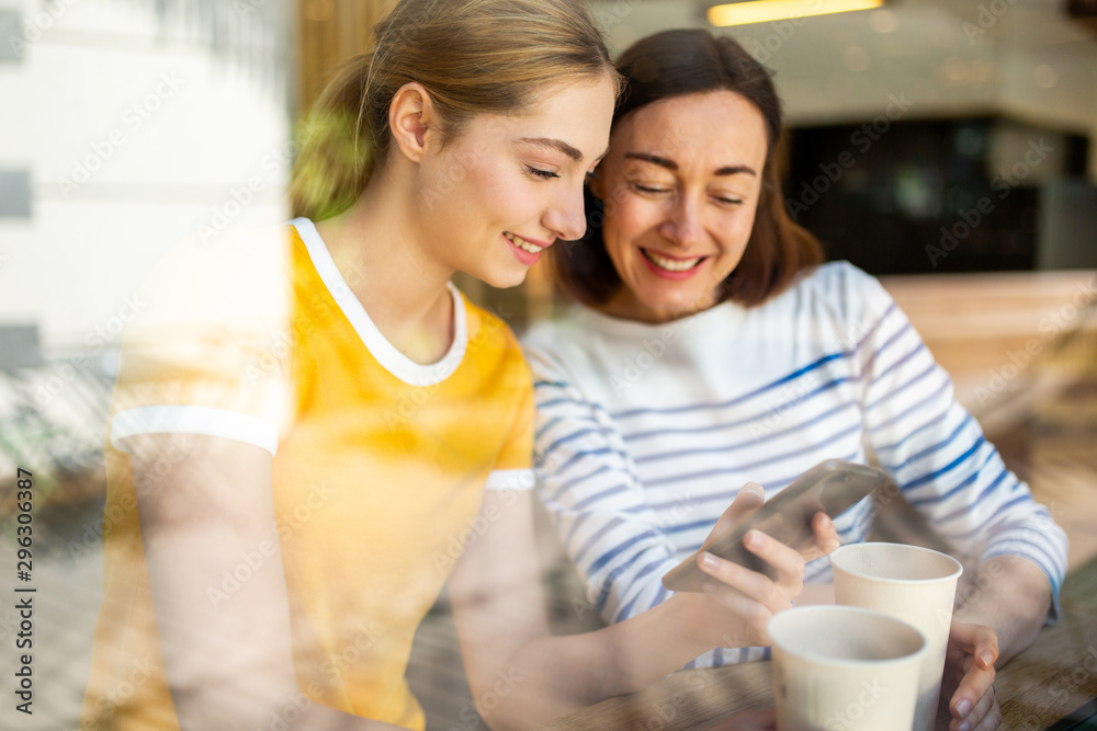 smiling mother and daughter sitting at cafe together looking at mobile phone smiling mother and daughter sitting at cafe together looking at mobile phone