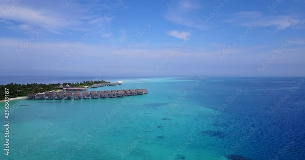 Aerial view approaching docks and houses at a resort in the Maldives, situated on crystal clear blue waters and the beach Aerial view approaching docks and houses at a resort in the Maldives, situated on crystal clear blue waters and the beach