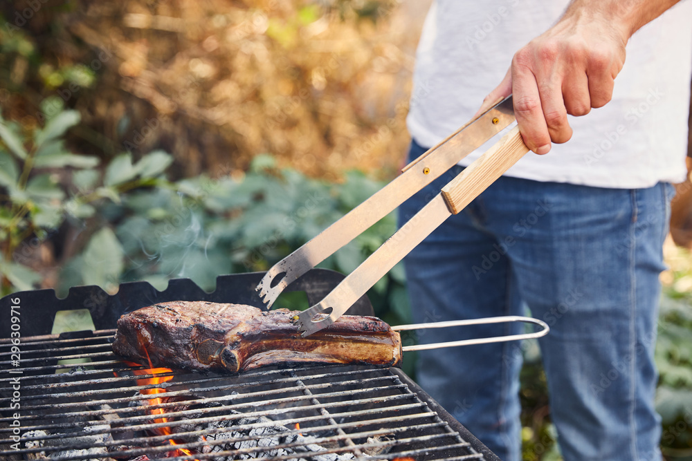 Fototapeta premium cropped view of man with tweezers grilling meat on barbecue grid