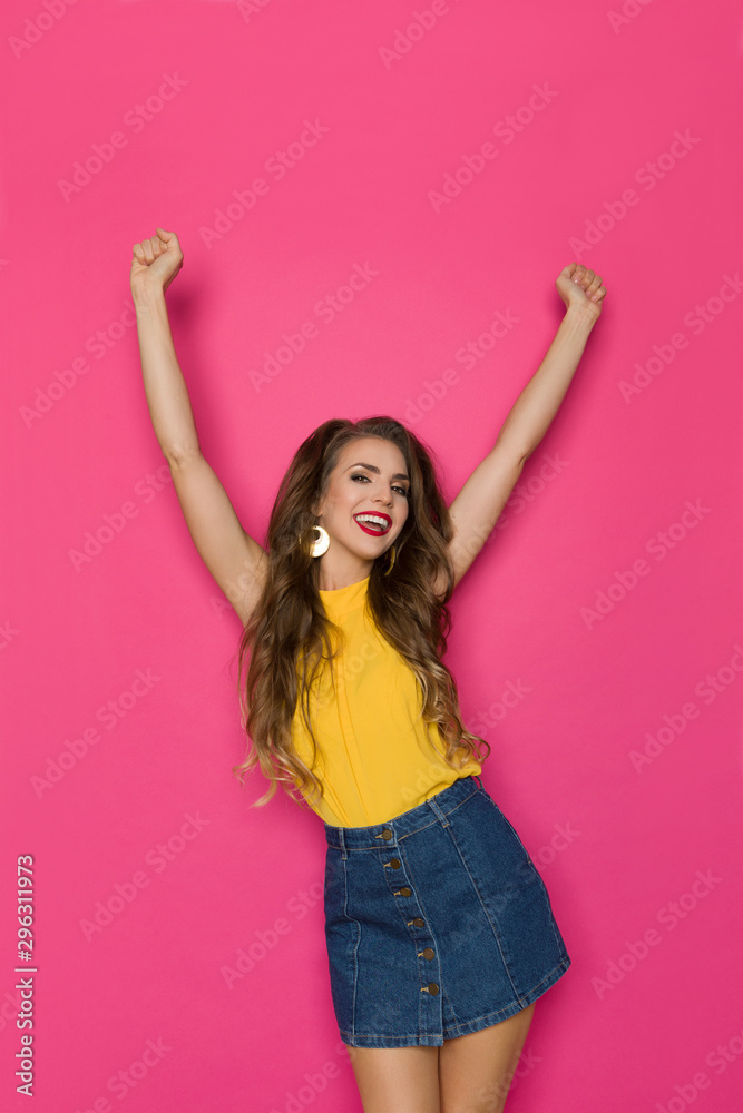 Young Woman In Jeans Mini Skirt And Yellow Top Is Standing With Arms Raised, Cheering And Shouting