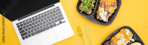panoramic shot of eco packages with vegetables, meat, fried eggs and salad, laptop, plastic fork and knife isolated on yellow