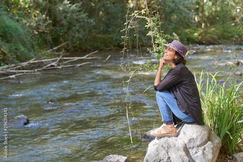  Latin brunette woman sitting on the bank of a river resting and taking a sun bath.