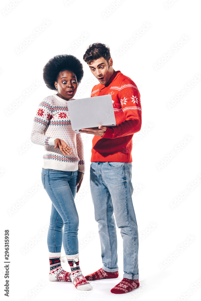 surprised multicultural couple in sweaters using laptop, isolated on white surprised multicultural couple in sweaters using laptop, isolated on white