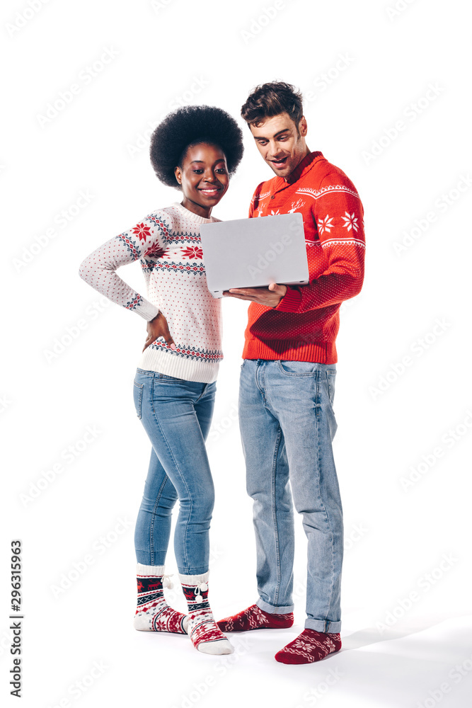 beautiful multicultural couple in sweaters using laptop, isolated on white beautiful multicultural couple in sweaters using laptop, isolated on white