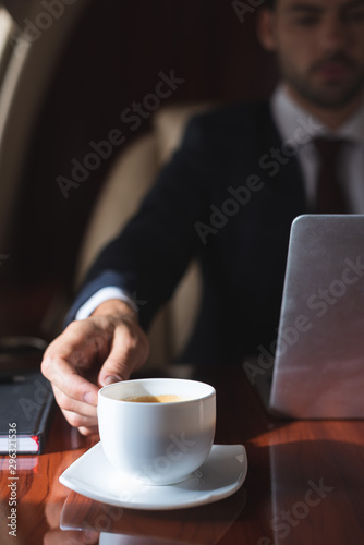 selective focus of businessman holding cup of coffee in plane with laptop