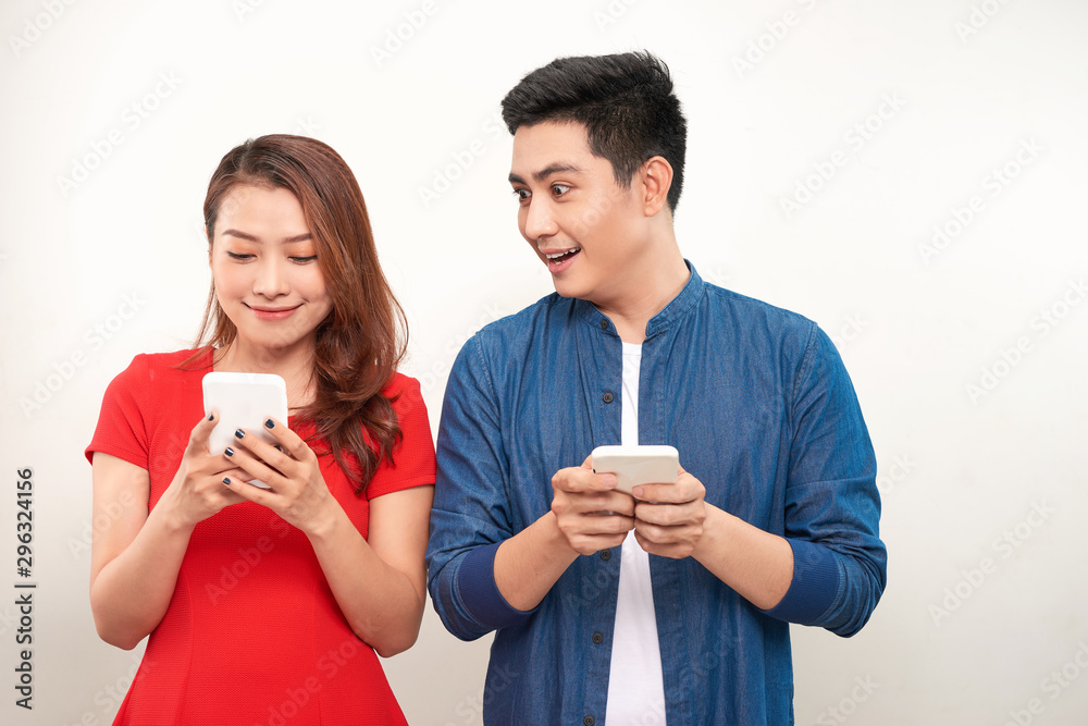 Asian couple using gadgets: pretty girl typing a message on cell phone while her boyfriend standing next to her, looking down at the screen of her smart phone Asian couple using gadgets: pretty girl typing a message on cell phone while her boyfriend standing next to her, looking down at the screen of her smart phone