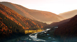 River in mountain valley covered with autumnal colorful forest at sunrise
