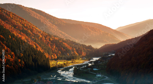 River in mountain valley covered with autumnal colorful forest at sunrise © okostia