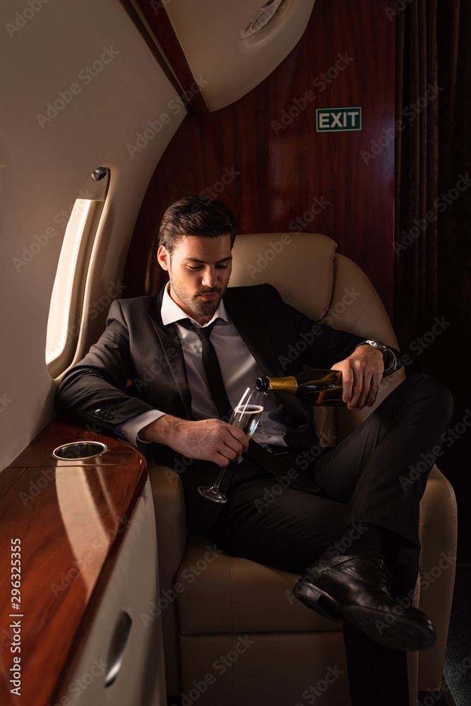 handsome man pouring champagne into glass in plane