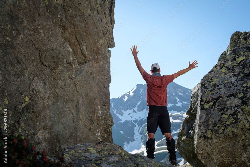 A hiker stands between two rocks and raises his hands