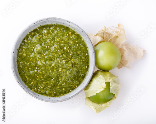 Tomatillo salsa verde. Bowl of spicy green sauce on white table, mexican cuisine. Top view.