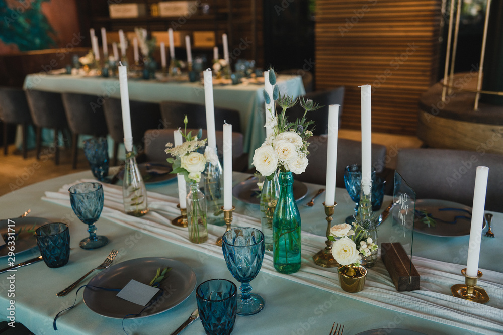 Coziness and style. Modern event design. Table setting at wedding reception. Floral compositions with beautiful flowers and greenery, candles, laying and plates on decorated table. - obrazy, fototapety, plakaty 