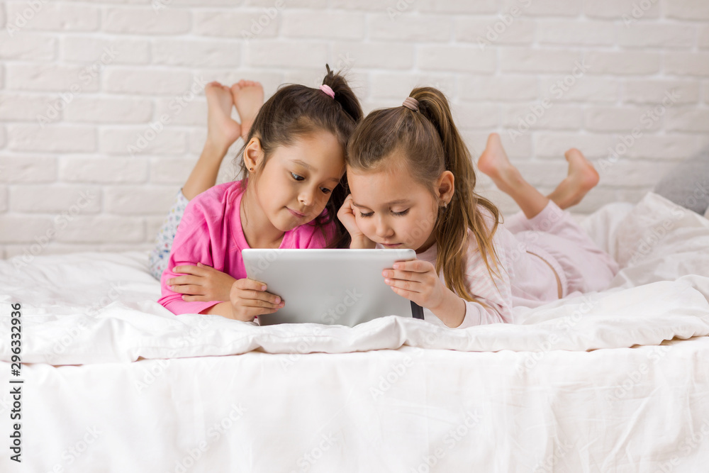 two cute children girls use digital tablet in bed. child playing on tablet pc.