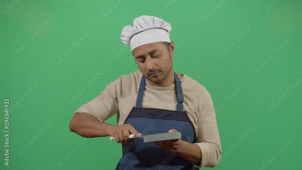 Knife Sharpening By A Funny Adult Man Cook. Studio Isolated Shot Against Green Screen Background