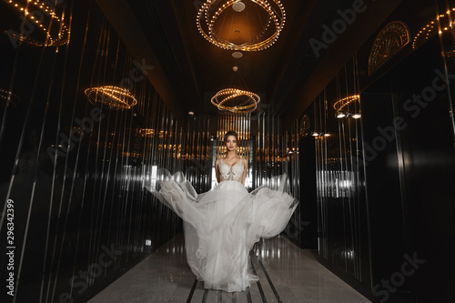 Beautiful leggy model girl in a wedding dress walking through the dark hall in a luxurious restaurant. Young woman bride in modish dress. Concept of wedding fashion.