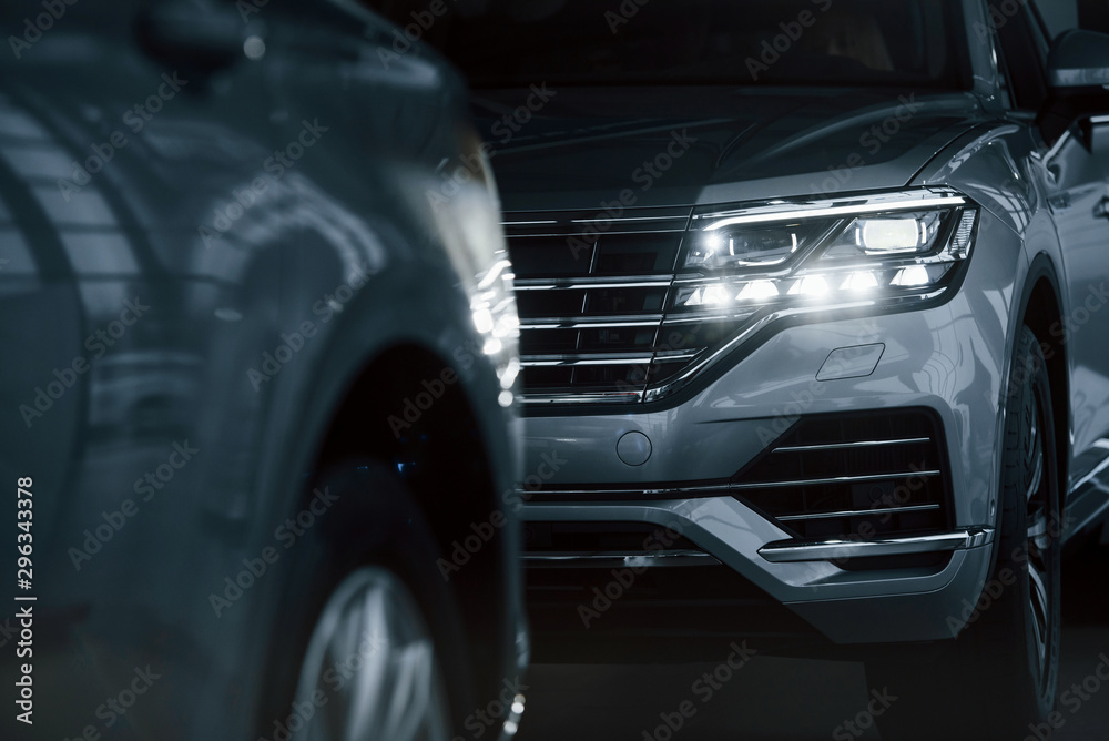 Powerful headlights. Particle view of modern luxury cars parked indoors at daytime