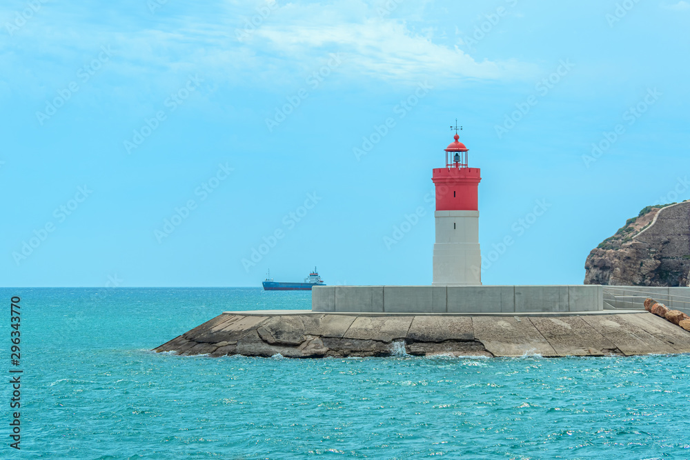 Red and white lighthouse at sea and ship on the horizon near The city of Cartagena, Spain. Red and white lighthouse at sea and ship on the horizon near The city of Cartagena, Spain.
