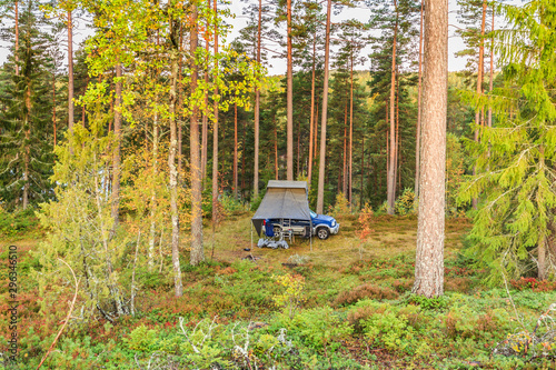 Wild camping in Sweden with 4x4 terrain car and roof tent in a natural forest at the foot of a hill with beautiful autumn colors in the warm light of the setting sun and far from habitation