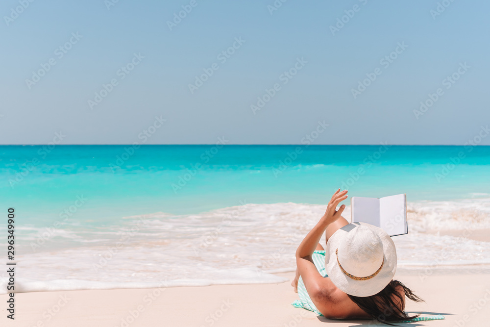 Fototapeta premium Young woman reading book on chaise-lounge on the beach