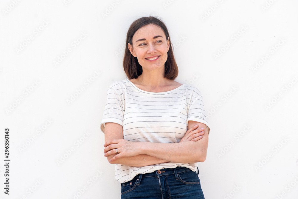 Fototapeta premium smiling older woman standing by white background with arms crossed and glancing