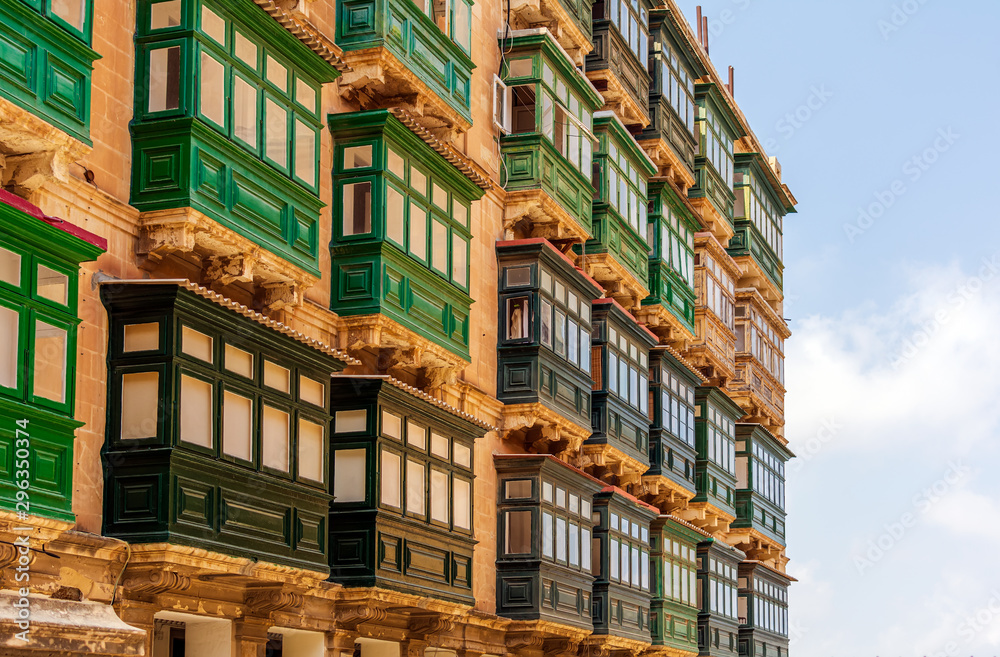 Residential house facade with traditional Maltese green wooden enclosed balconies in Valletta, Malta, in evening sunlight. Authentic Maltese urban scene.